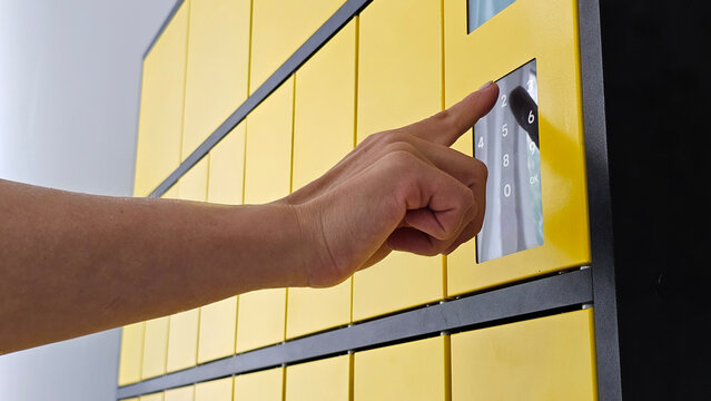 Person entering code on a touch screen of a yellow automated parcel locker close-up.