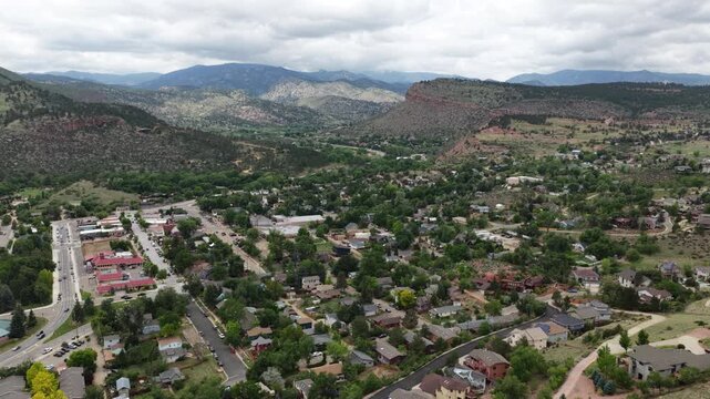 Aerial of small town nestled in mountain valley Lyons Colorado in spring with dense residential and commercial development mature trees rolling forested mountains and overcast cloudy sky