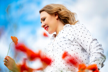 Fototapeta premium Content woman in polka dot blouse looking down at red poppy flower. Concept of mindfulness and appreciation of natural beauty.