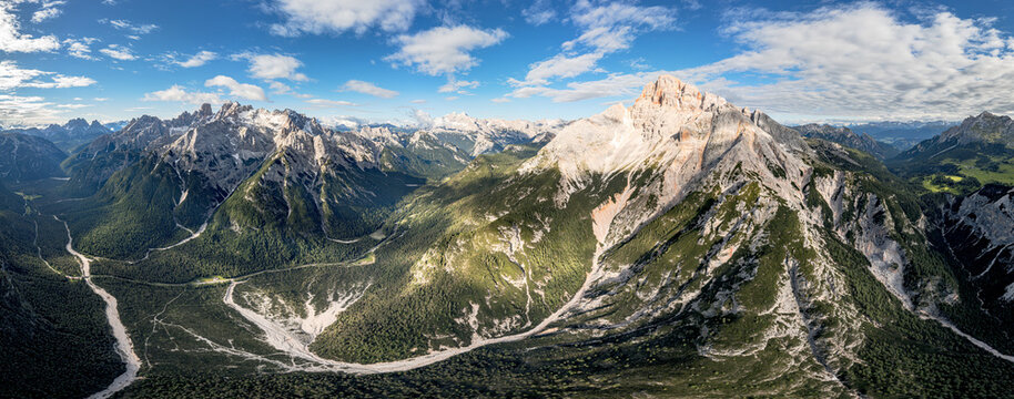 Aerial view of the majestic peaks of Prato Piazza and the surrounding Dolomites with a winding valley and lush green slopes under a blue sky Dobbiaco, Trentino-Alto Adige, Italy.