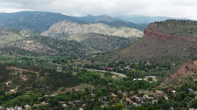 Aerial of residential community nestled in mountain valley in Lyons Colorado with dense forestation winding roads and prominent red rock cliffs in front range Rocky Mountains