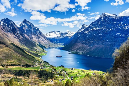 View of the village of Urke in the Hjorundfjord in Norway with mountains, a ship, and green fields on a sunny day