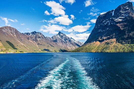 View from the stern of a ship toward the mountains at the horizon in Norway