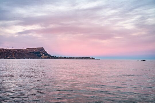 Scenic view of the water under a pink sky in Norway with distant cliffs and a quiet shoreline during sunset