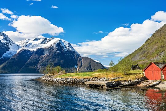 Lakeside or sea view in Norway with mountains, blue sky, and house by the water during a sunny day in spring or summer