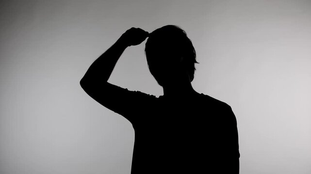 An anonymous silhouette of a man stands against a white wall and combs his hair