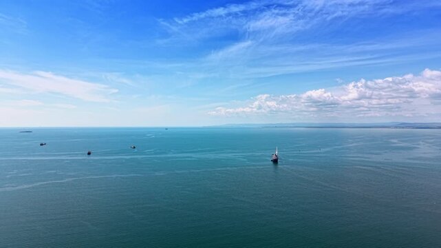 Multiple vessels anchored in open waters near Burgas port, Bulgaria. Elevated drone view of scattered ships on teal sea with cumulus clouds above.