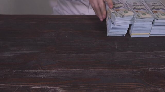 A businessman in a business suit takes a wad of cash dollars closer to himself and puts it next to a stack of other money