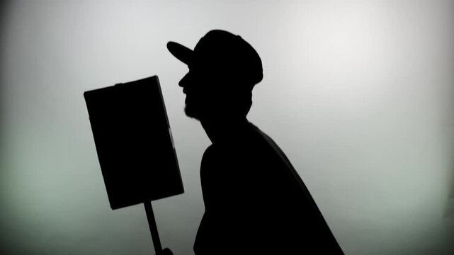 An anonymous silhouette of a man in a cap walks with a protest poster on a white background