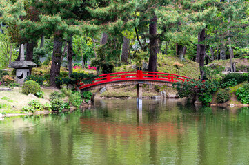 Fototapeta premium Traditional red wooden arched bridge over a peaceful pond in an oriental garden