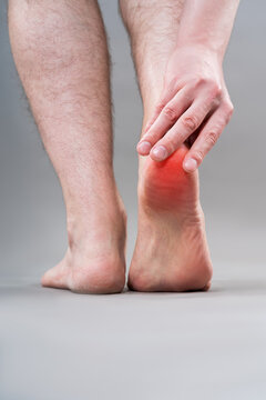 Heel pain, plantar fasciitis or achilles tendinitis concept. Rear view of man holding his aching foot with red inflammation graphic