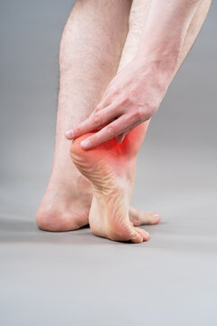 Heel pain, plantar fasciitis or achilles tendinitis concept. Rear view of man holding his aching foot with red inflammation graphic