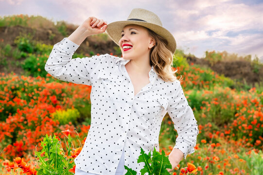 Confident blonde woman in straw hat and white shirt smiling in poppy field. Beautiful summer portrait in floral landscape highlighting natural charm and style.