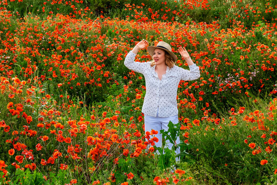 Carefree woman raises arms above scarlet poppy plants. Absolute freedom, vibrant summer energy.