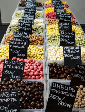 Colorful selection of gourmet coated nuts and candied fruits neatly organized in clear plastic trays. Varieties include almonds with chocolate, basil, and coconut flavo
