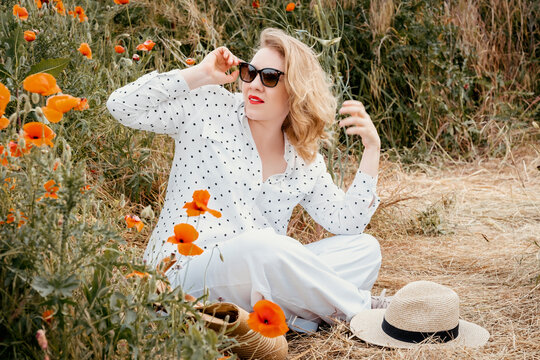 Happy woman sits on ground in poppy meadow. Vacation leisure, authentic joyful emotions.
