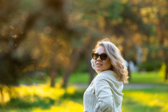 Stylish woman glances back in summer park. Chic vacation vibe, natural beauty confidence.