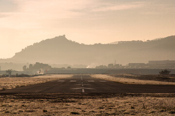 Airport runway extending towards distant foggy mountain castle © Valenti