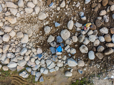 Aerial view of workers moving large river stones and boulders on a dry riverbed with sandy soil in Karanglewas, Central Java, Indonesia.