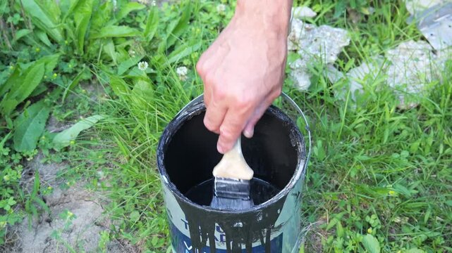Hand dipping paintbrush into black paint can