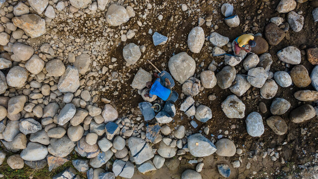 Aerial view of workers manually breaking large stones and boulders in the rocky terrain of Babakan in Karanglewas, Central Java, Indonesia.