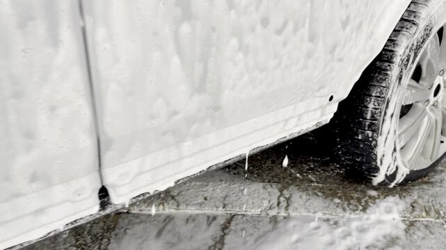 Process of spraying foam on the auto body in the station. Second phase of detailing washing in car service. Car washer does full body car wash with soap. Cleaning the car using high pressure water. 