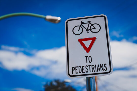 A small rectangular sign indicating cyclists need to give way to pedestrians, signalling cyclists commonly travelling at high speed and need to pay attention to people walking and crossing the street.