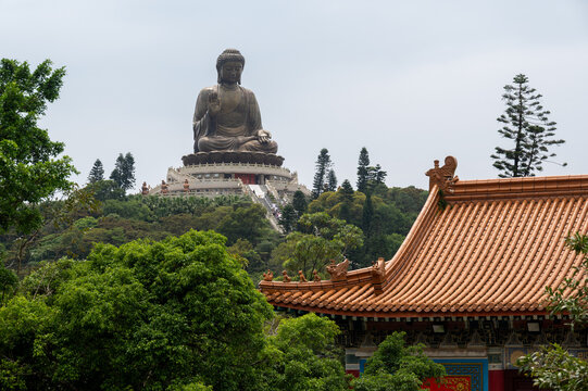 The giant Tian Tan Buddha bronze statue on a hill framed by traditional temple roofs on Lantau Island, Hong Kong