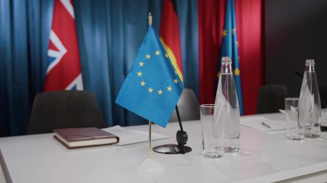 European Union flag standing on conference table with international flags in background. Footage is ideal for news broadcasts, political reports, and international relations videos close up
