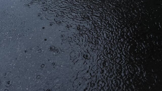 Raindrops falling on the dark black asphalt road, top view rain on gloomy autumn day dark black asphalt road, top view rain on gloomy autumn day. Background, texture of drops
