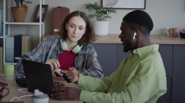 Medium shot of Caucasian young adult woman and African American young adult man discussing work on laptop in office. Video perfect for tech startup promotions and corporate training videos