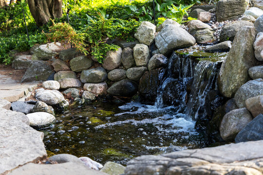 Small rocky waterfall feature with rocks and splashing stream in botanical garden pond. Mini cascade waterfall flowing over stones in park. Ornamental Gardens in Ottawa, Canada