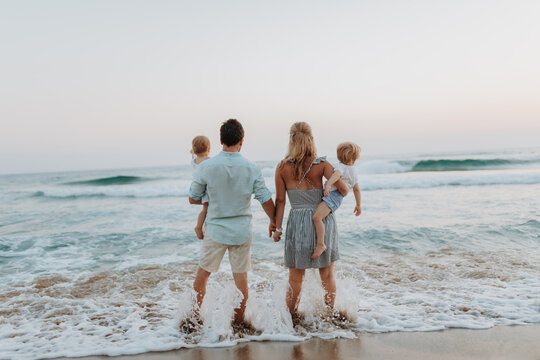 A family with two toddler children walking on beach on summer holiday at sunset.