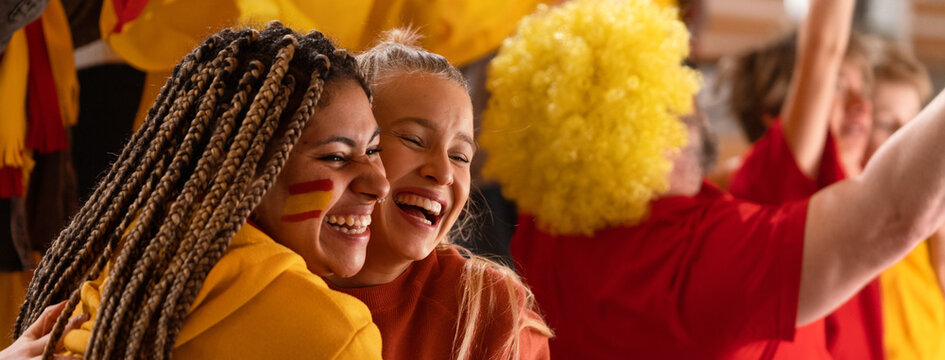 Happy football fans supproting Spanish national team in live soccer match at stadium, celebrating.