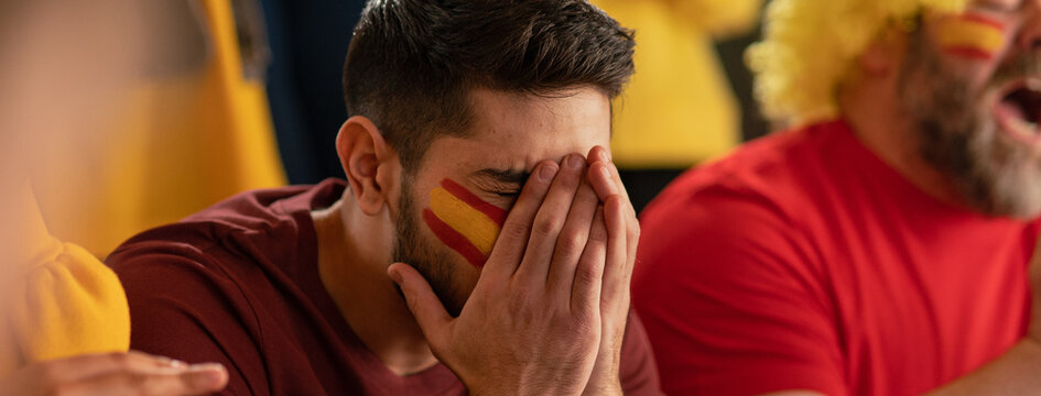 Worried football fans supporting spanish national team in live soccer match at stadium.