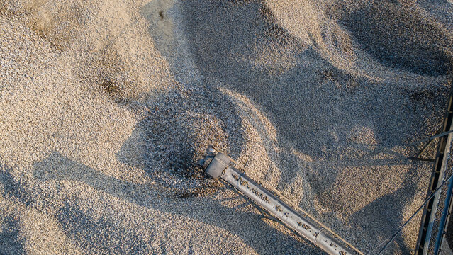 Aerial view of a conveyor belt pouring crushed stone onto large gravel piles at an industrial site in Karanglewas, Central Java, Indonesia.
