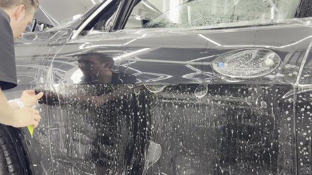 A car wrapping specialist applies a polyurethane film to the car. Detailer smoothes PPF. Car wrapping, detailing, tuning and styling. PPF protective film against chips and scratches. 