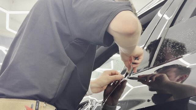 A car wrapping specialist applies a polyurethane film to the car. Detailer smoothes PPF. Car wrapping, detailing, tuning and styling. PPF protective film against chips and scratches. 