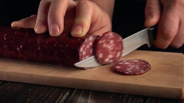 Slicing cured sausage on wooden cutting board with sharp knife, showcasing the continuous action of cutting through the meat
