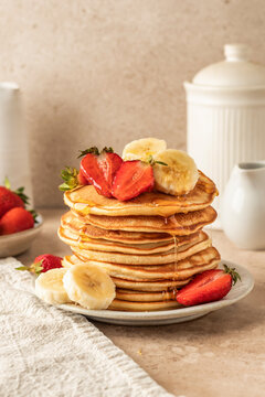Pancakes with banana and strawberry on beige table background. Morning food, summer breakfast. Pancake day or Maslenitsa recipe