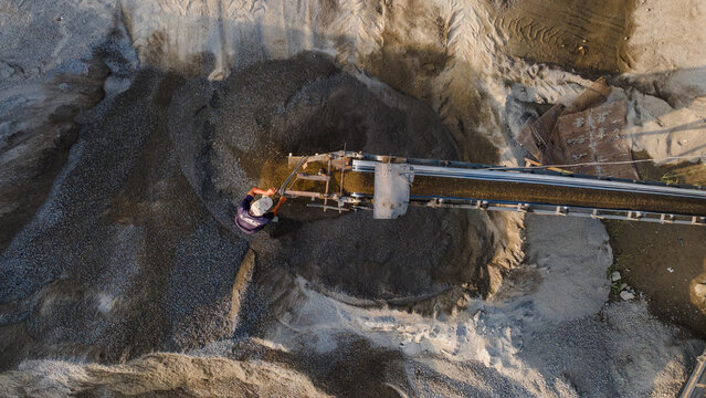 Aerial view of a worker operating a conveyor belt at a sand quarry with piles of gravel and earth in Karanglewas, Central Java, Indonesia.