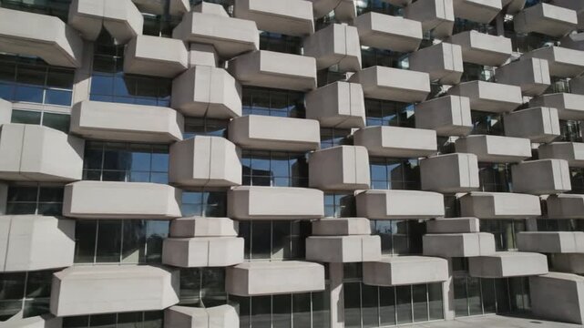Modern architectural facade featuring repeating geometric concrete modular blocks and glass window panels reflecting the sky. Structured design creates rhythmic texture on building exterior.
