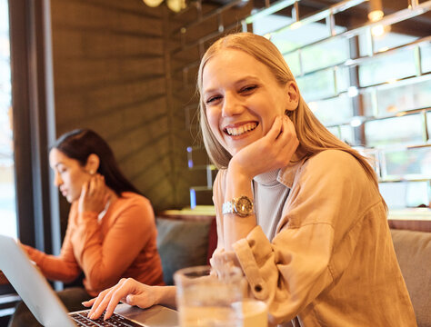 Woman smiling, holding coffee while working on a laptop having an online meeting conferance call  in a cafe