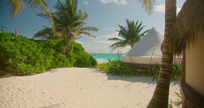 Luxury tent sits on sand surrounded by palm trees at Tulum beach resort Mexico