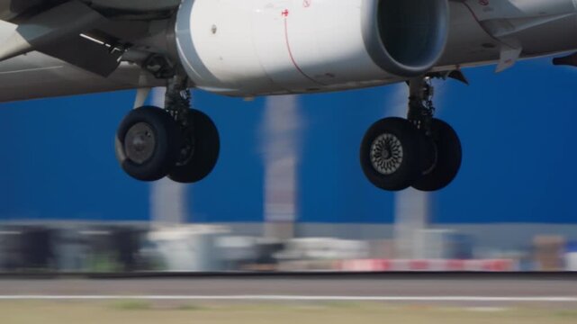 Extreme close up of commercial passenger jet main landing gear and jet engine underbelly during takeoff or landing on airport runway, motion blur background, daylight.