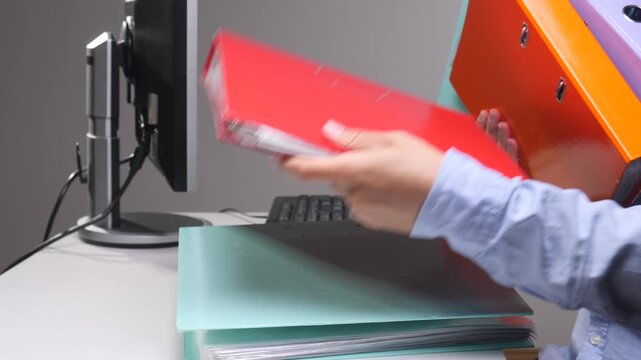 Person arranging a stack of colorful ring binders on a desk, representing the concept of organization, data management, archiving, documentation, and office workload in a corporate environment