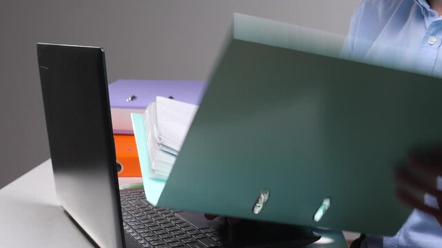 Person's hand carrying a large stack of colorful office binders and paper documents, representing heavy workload, administration, and bureaucracy in a professional setting