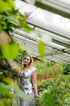 Woman stands in a garden wearing a shiny outfit surrounded by green plants and flowers