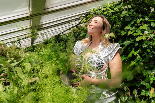 Woman holds plant in greenhouse while enjoying light from above in warm weather