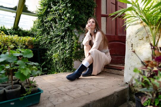 Woman sits on steps near plants in greenhouse on a sunny day enjoying the moment